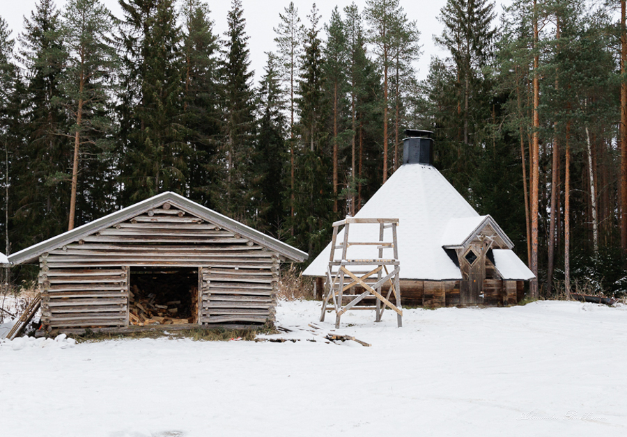 Jokikylän kylätalon kota kuvattuna talvella etuviistosta. Vasemmalla etualalla on puuvaja ja kauempana oikealla kota. Takana näkyy kangasmetsää.