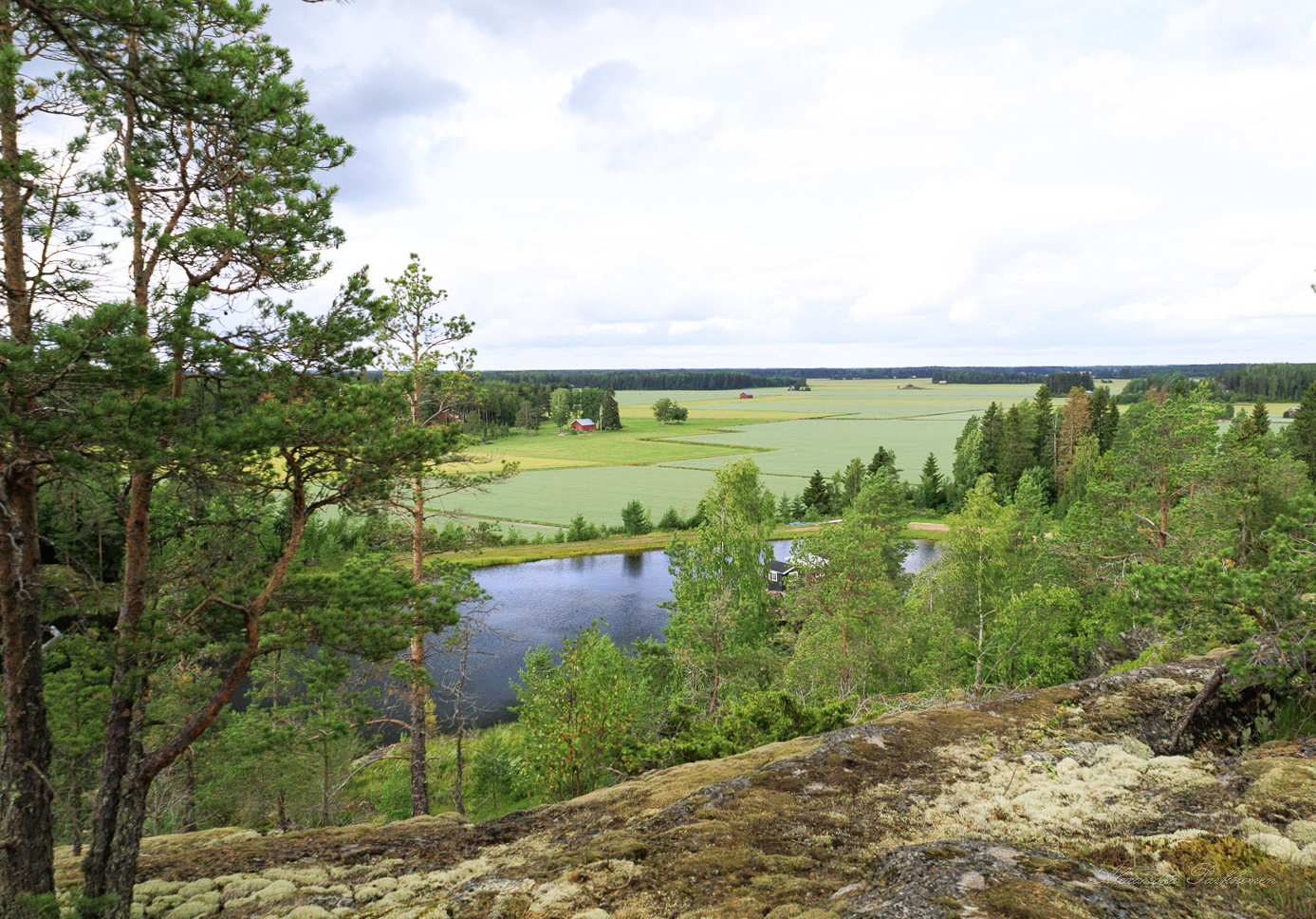 Kallion päältä otettu maisemakuva. Etualalla näkyy kalliota, horisontissa joki sekä peltoa.