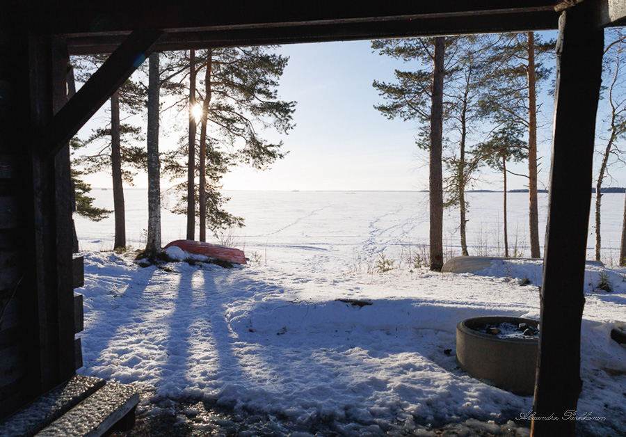 Laavun sisältä ulospäin otettu kuva, jossa näkyy laavun nuotiopaikka sekä järvimaisema.