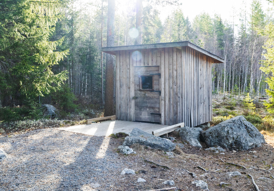 Puinen esteetön käymälä metsässä. Käymälärakennuksen edessä on puinen ramppi.