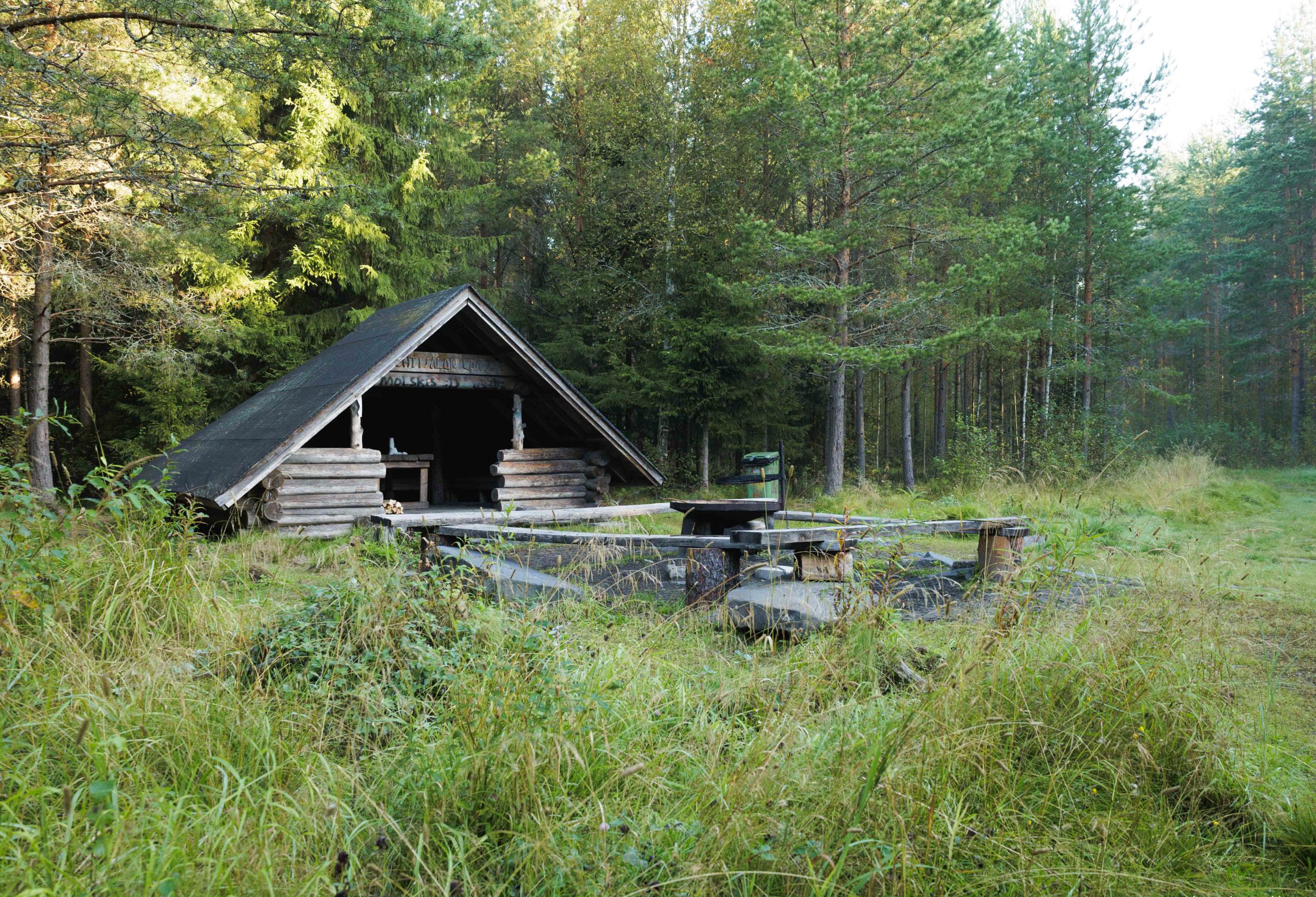Metsän reunalla sjaitseva laavu kuvattuna etuviistosta. Laavun edustalla näkyy puisin penkein reunustettu nuotiopaikka.