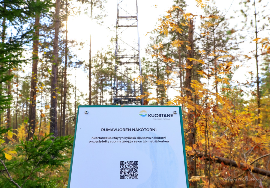 Näkötornin edessä olevasta opastetaulusta otettu kuva. Opastetaulun takana näkyy näkötorni sekä metsää.