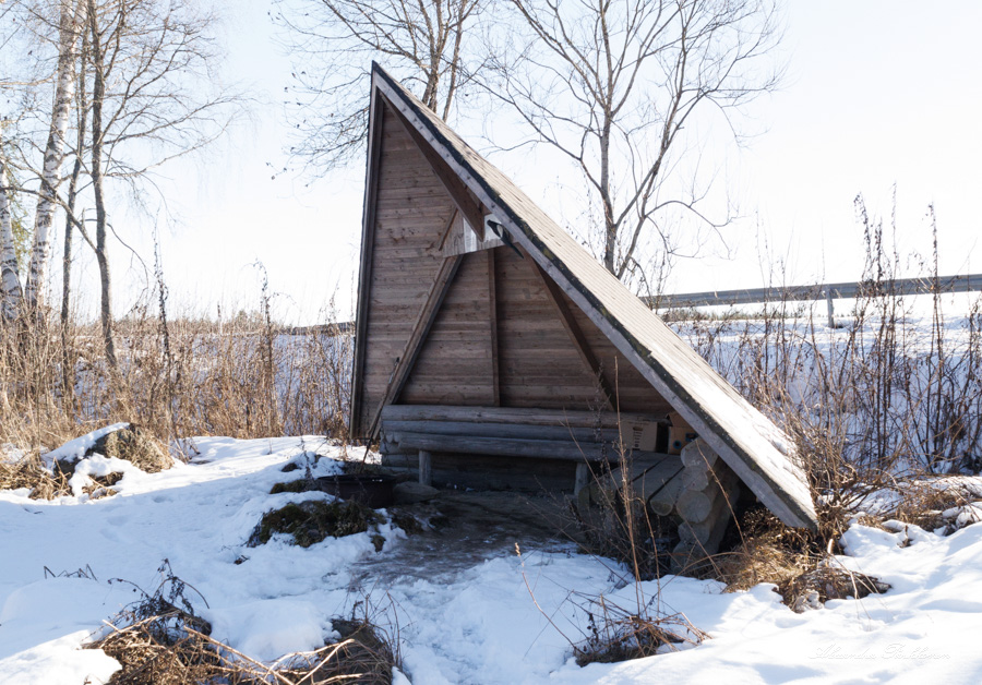 Tien vieressä sijaitseva laavu kuvattuna etuviistosta talvella. Laavun edustalla näkyy nuotiopaikka sekä lunta. Laavun takana on puita.
