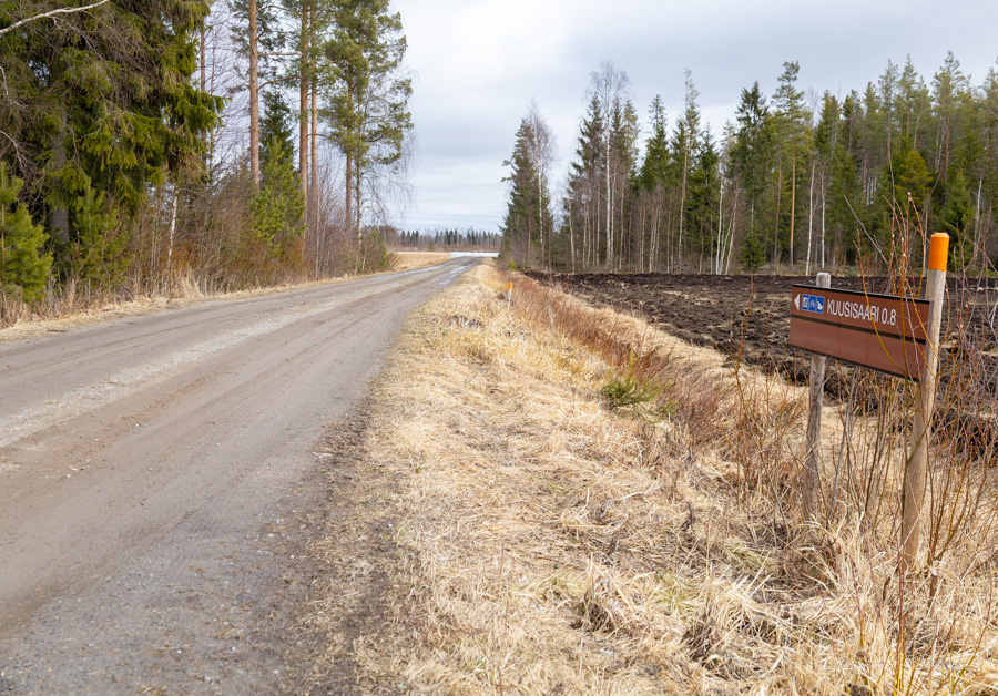 Retkeilyreitin ruskea opastekyltti tien vieressä. Ympärillä näkyy metsää.