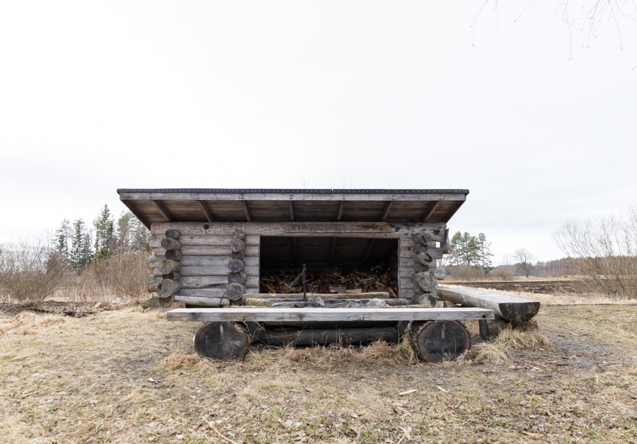Puinen laavu kuvattuna edestäpäin. Laavun edessä on puisin penkein reunustettu nuotiopaikka.